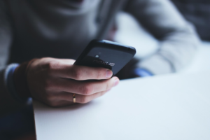 Une personne tient un smartphone noir au-dessus d’une table claire